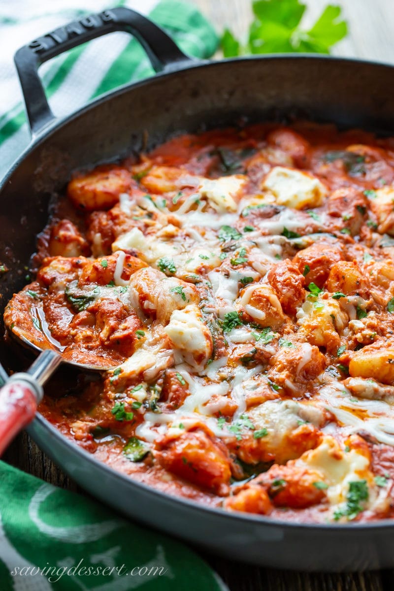 A skillet of baked tomato gnocchi with ricotta and mozzarella garnished with parsley
