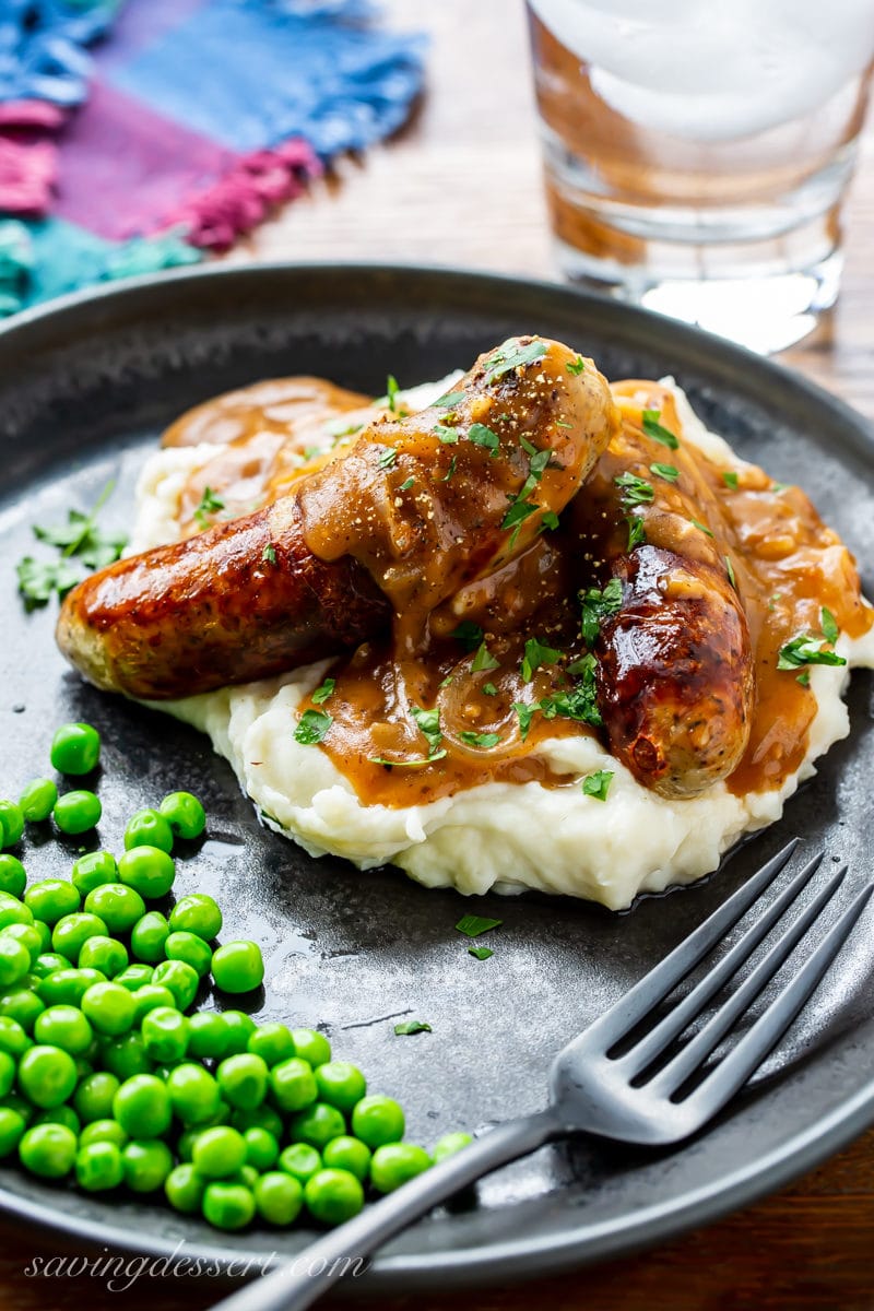 A plate of bangers and mash with onion gravy served with peas
