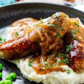 A plate of sausages with onion gravy over mashed potatoes