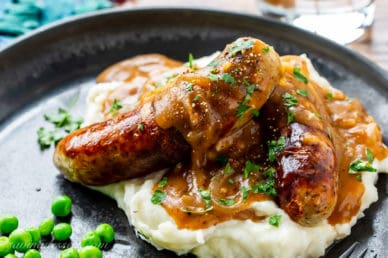 A plate of sausages with onion gravy over mashed potatoes
