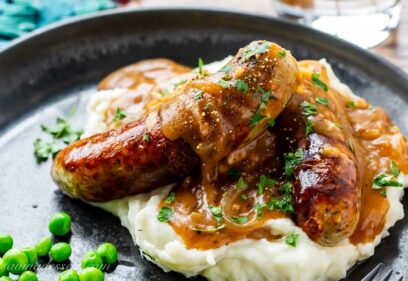 A plate of sausages with onion gravy over mashed potatoes