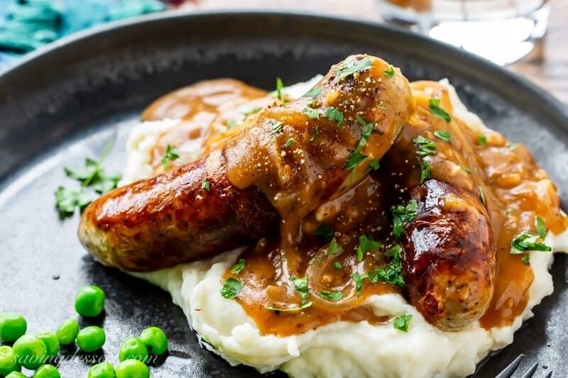 A plate of sausages with onion gravy over mashed potatoes