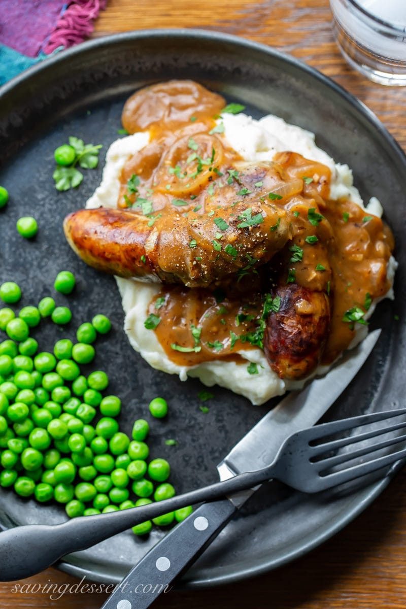 A plate of bangers and mash with peas and onion gravy