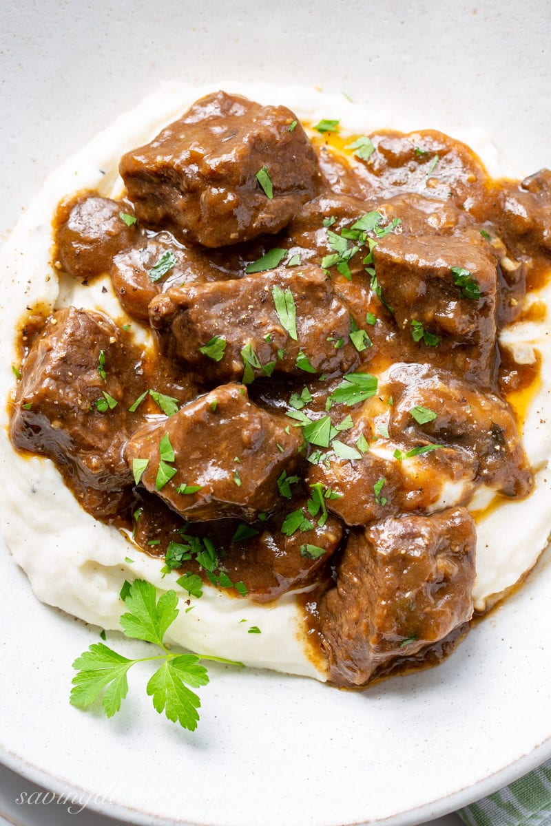 A bowl of tender Beef Tips and Gravy with mushrooms and onions served over fluffy mashed potatoes