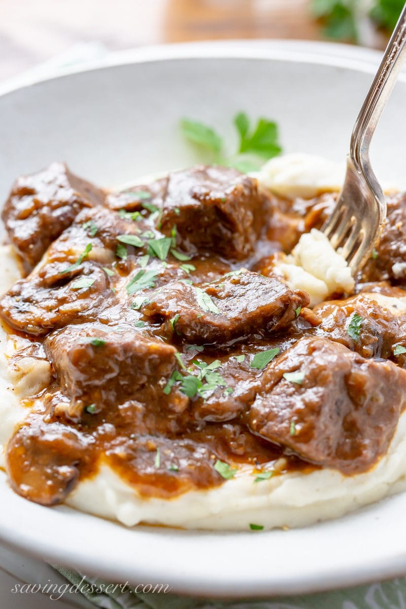 A bowl of mashed potatoes topped with tender Beef Tips in a rich, flavorful gravy filled with mushrooms and onions.