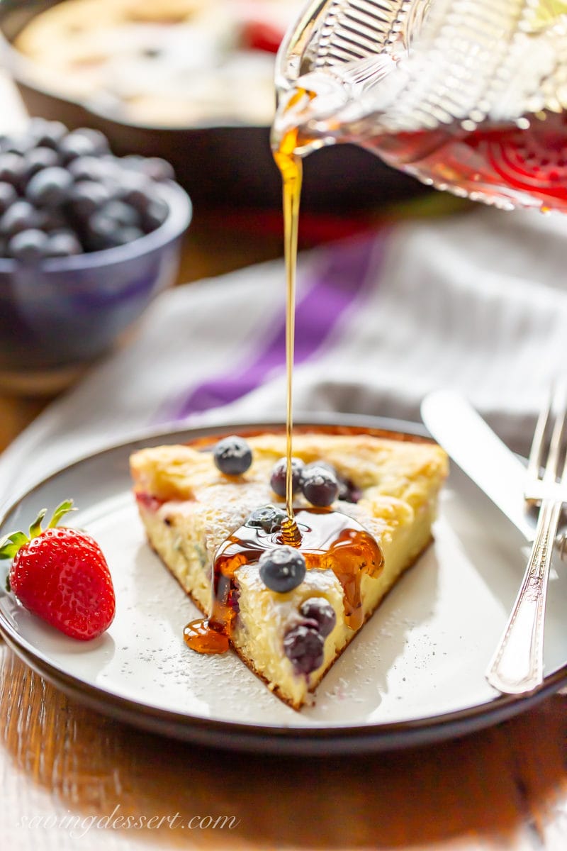 A slice of a skillet baked pancake being drizzled with syrup with strawberries and blueberries