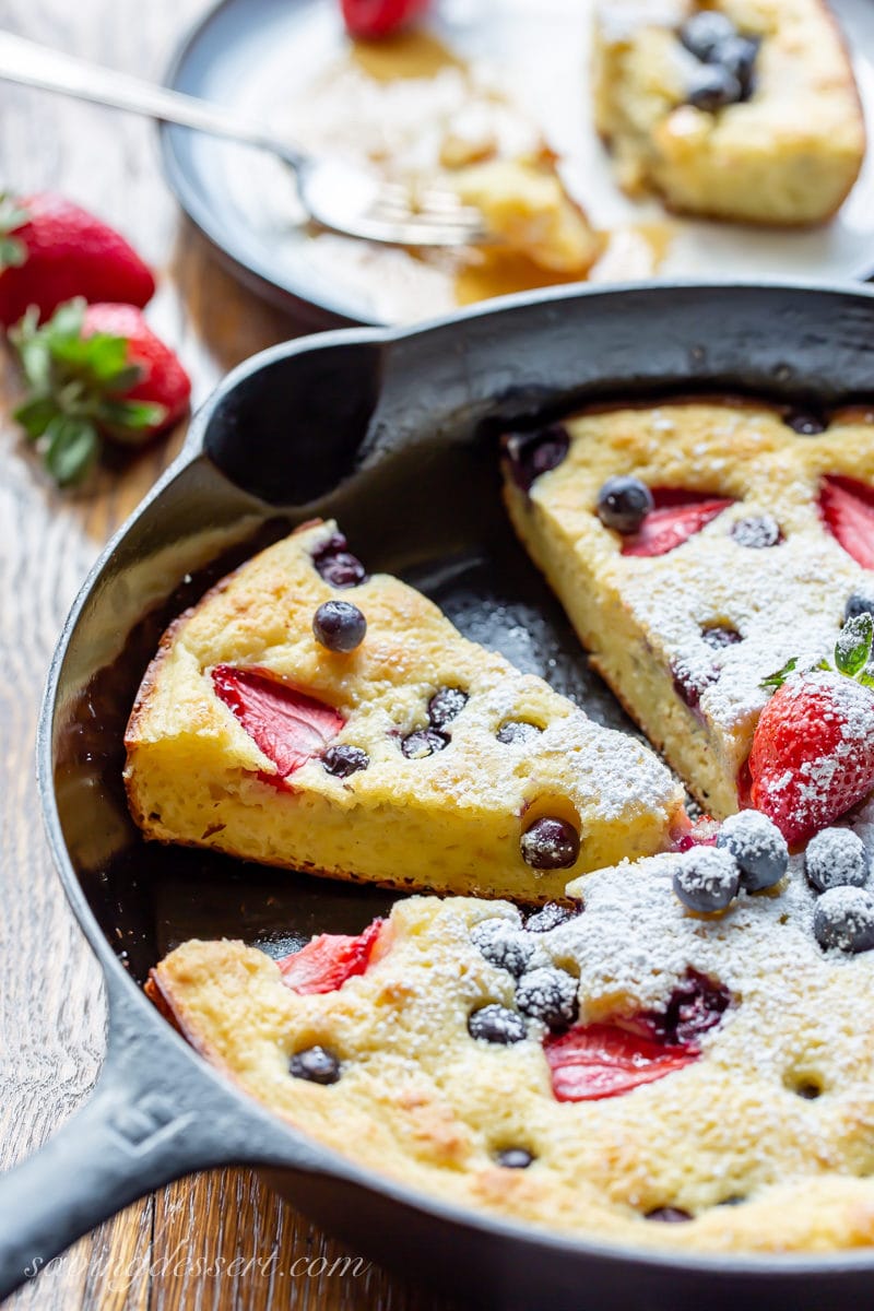 A cast iron skillet with a sliced berry buttermilk baked pancake with strawberries and blueberries