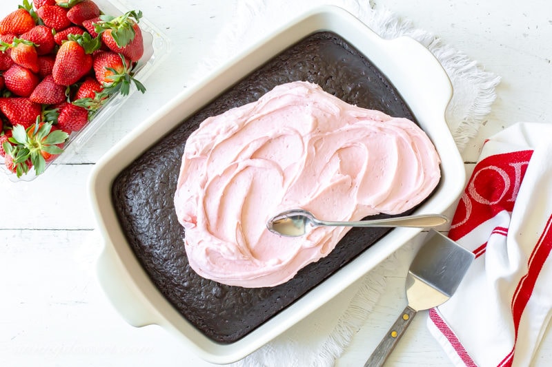 A pan of dark chocolate cake topped with fresh strawberry frosting