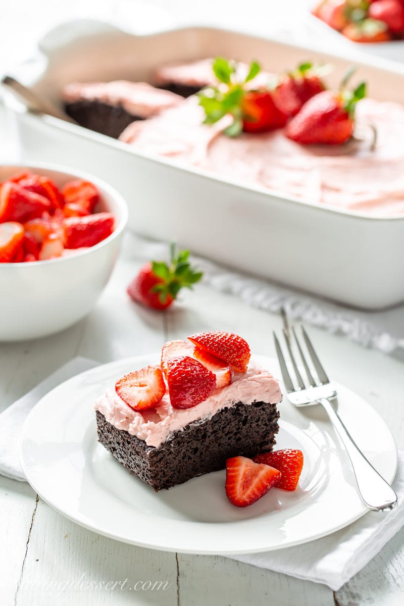A slice of dark chocolate sheet cake topped with strawberry frosting and served with fresh strawberries