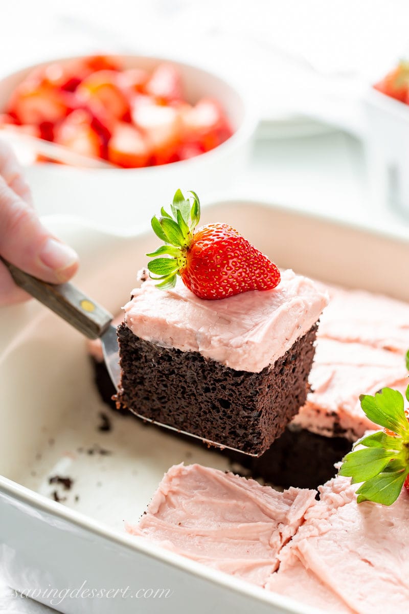 A slice of dark chocolate cake with strawberry frosting and fresh strawberries