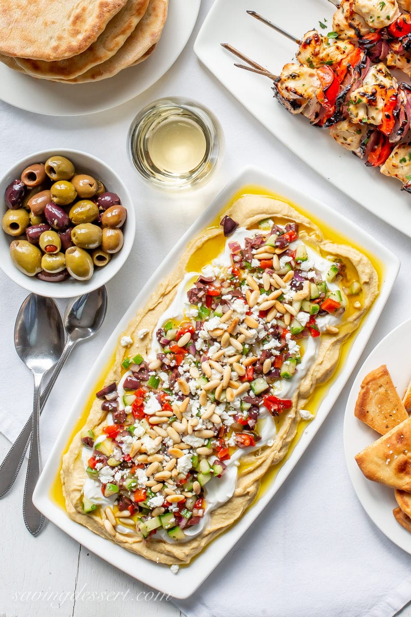 A platter of Greek Hummus Dip, olives, fresh pita bread and Greek marinated chicken kabobs