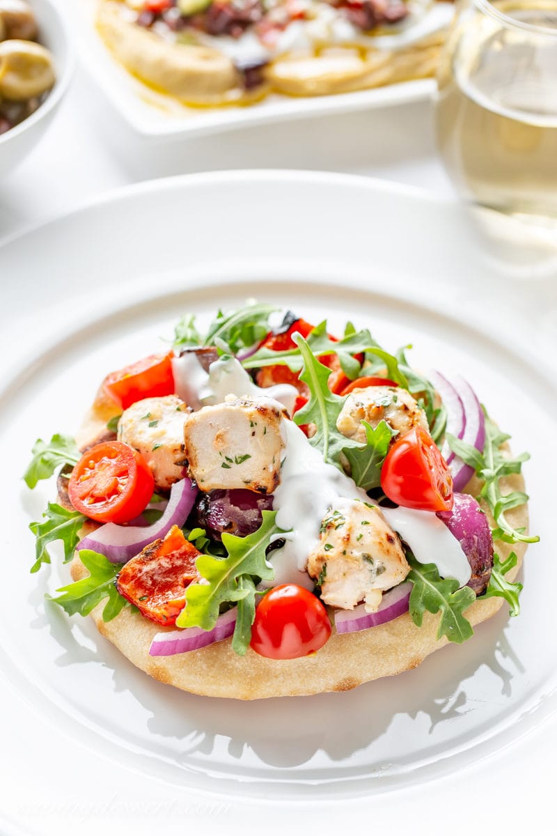 A grilled Greek Chicken pita pizza with arugula, onions and tomatoes