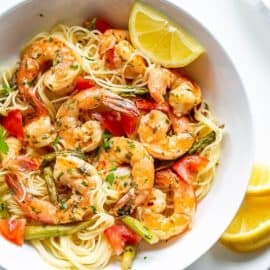 A bowl of shrimp scampi with tomatoes and asparagus over angel hair pasta