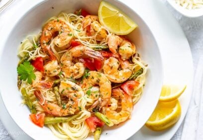 A bowl of shrimp scampi with tomatoes and asparagus over angel hair pasta