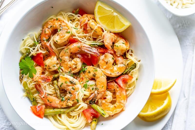 A bowl of shrimp scampi with tomatoes and asparagus over angel hair pasta