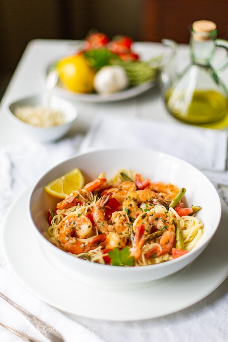 A table with a bowl of shrimp and pasta, olive oil and fresh vegetables