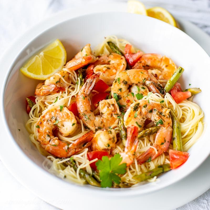 A closeup of a bowl of shrimp scampi with parsley and lemon garnish