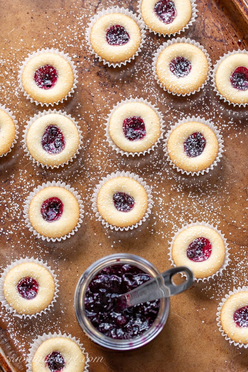 Almond Tea Cake Cookies with wild blueberry jam dusted with powdered sugar on a baking tray