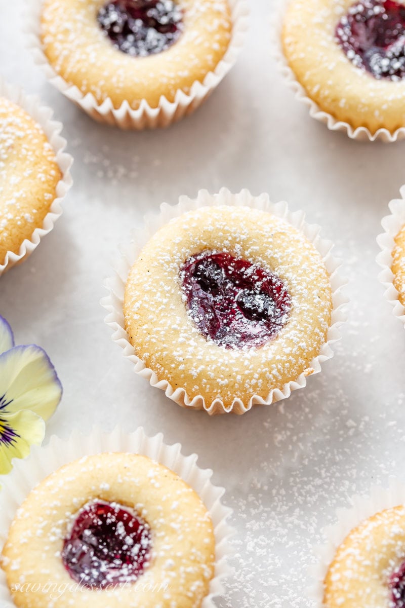 A close-up of almond tea cakes with wild blueberry jam and dusted with powdered sugar in mini paper cupcake liners 