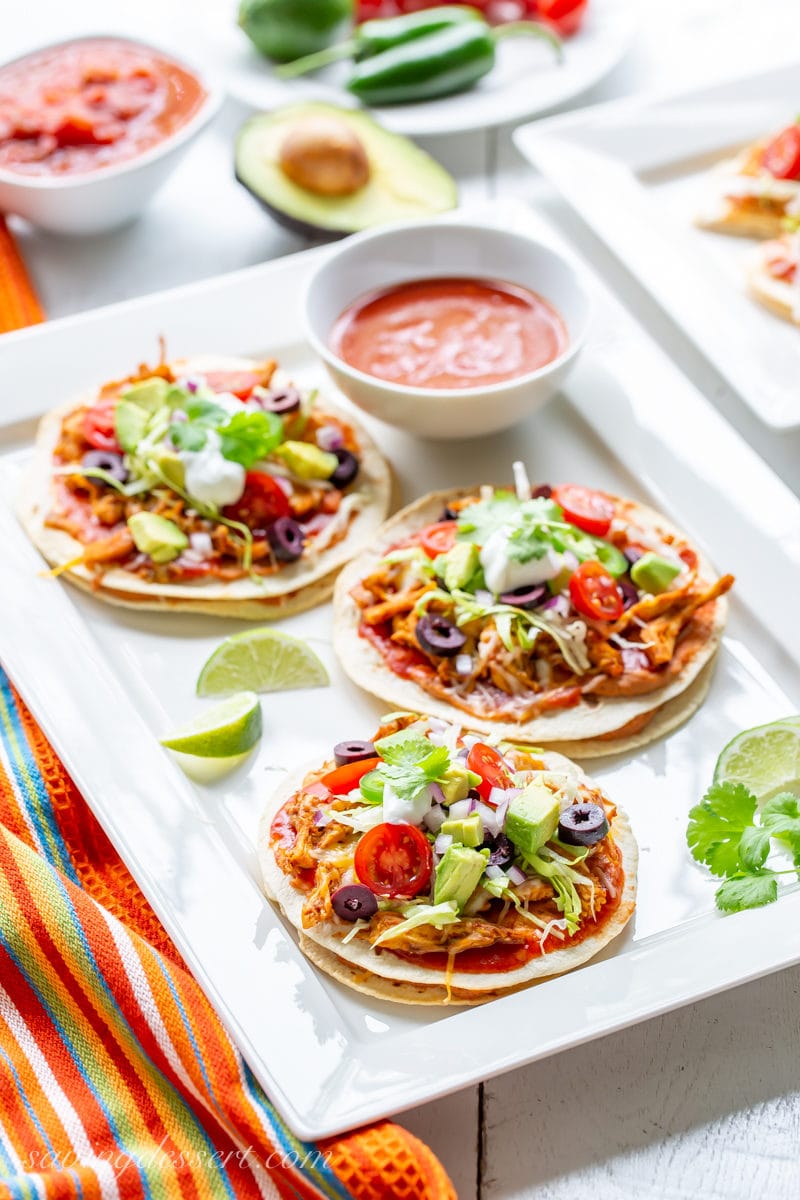 A platter of easy Mexican Pizzas topped with avocado, lettuce, tomatoes, onions and sour cream