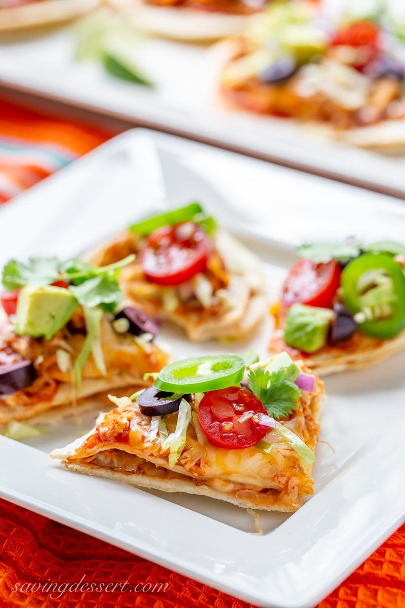 Nacho style Mexican Taco Pizzas with jalapeños, tomato, olives, lettuce and cilantro