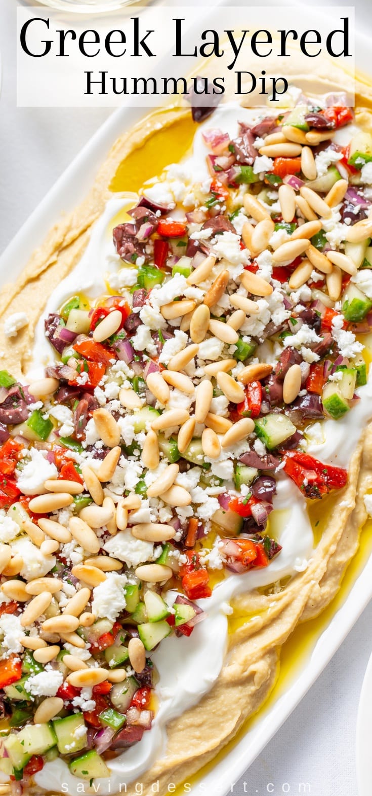 A platter filled with hummus dip topped with diced vegetables and pine nuts