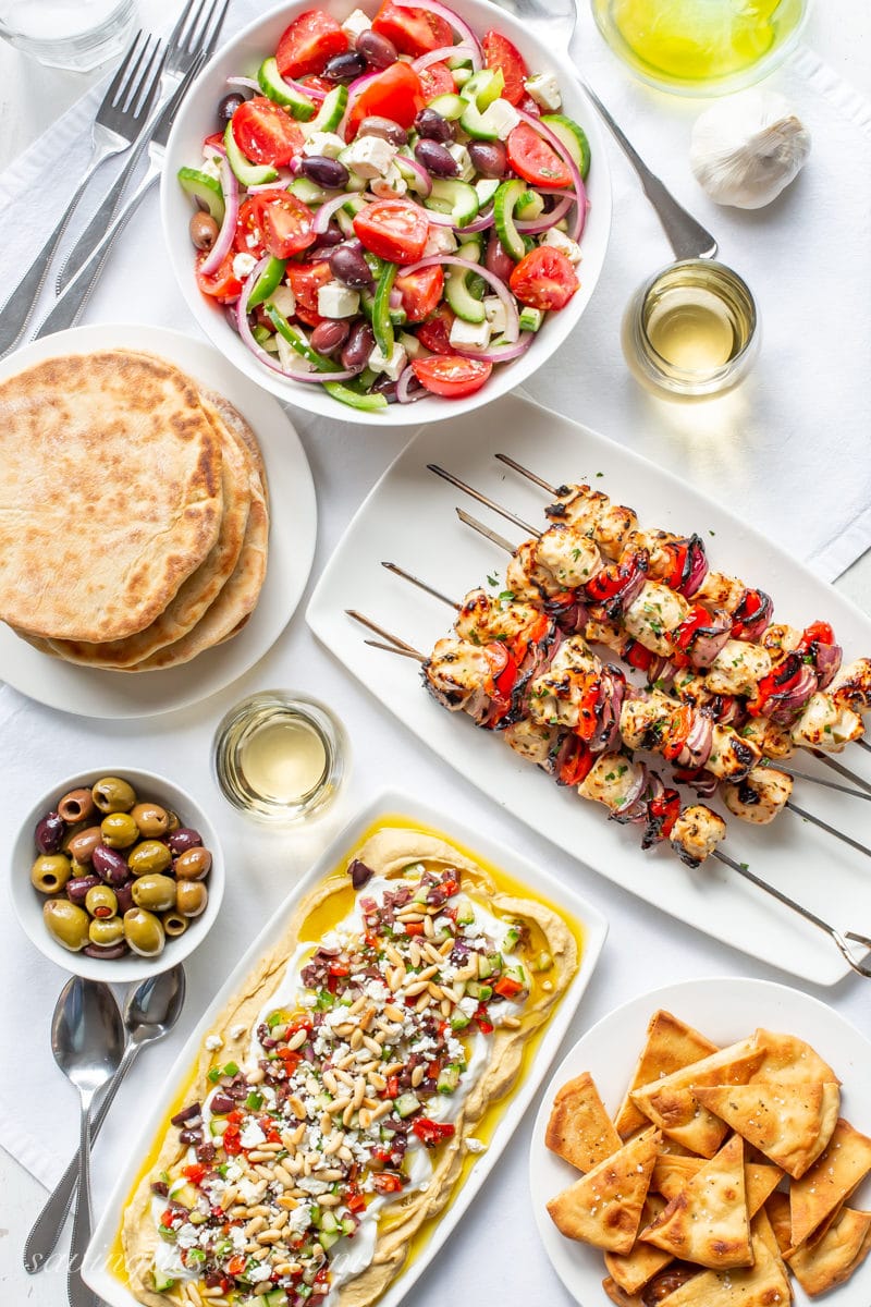 A Greek themed dinner party with whole wheat pita breads, pita chips, olives, wine, Greek salad, chicken kabobs and a layered Greek hummus dip