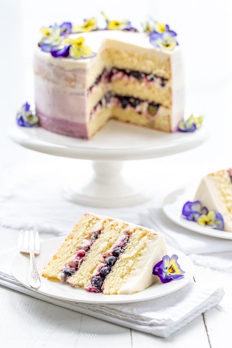 A sliced three layer lemon cake with blueberry filling garnished with blue and yellow pansies