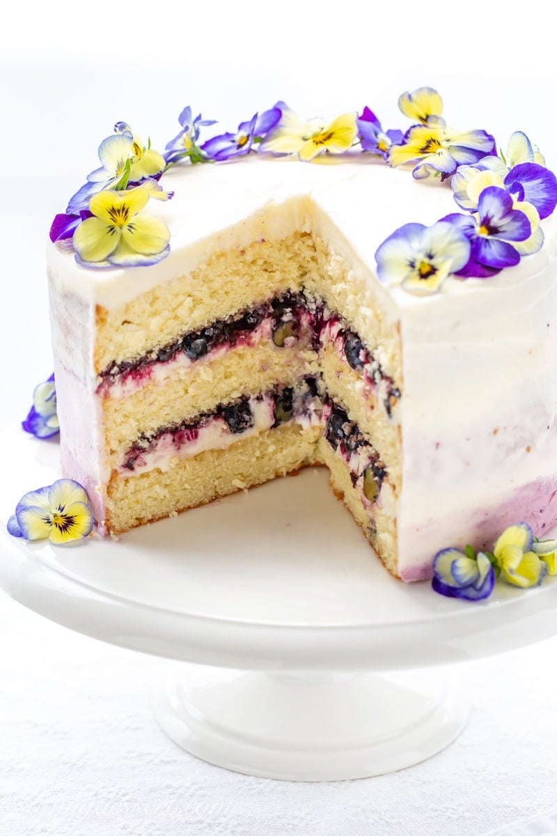 A three layer lemon cake with blueberry filling topped with edible blue and yellow pansies