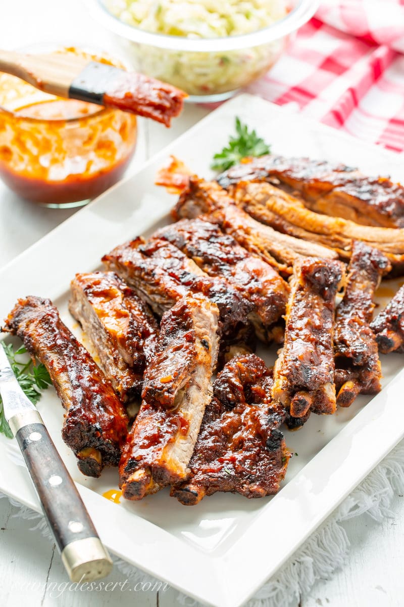 A large platter of barbecued pork ribs with barbecue sauce and cole slaw