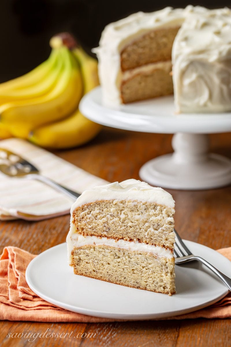 A slice of banana cake with bananas and the remainder of the cake in the background