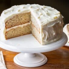 Front view of banana cake on cake stand with slice missing.