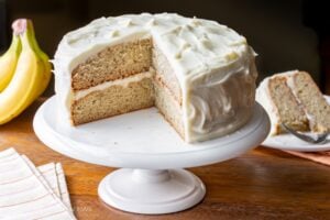 Front view of banana cake on cake stand with slice missing.