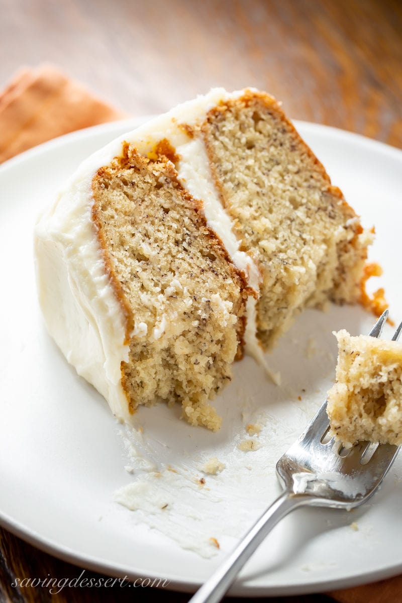 A close-up of a slice of banana cake with cream cheese frosting