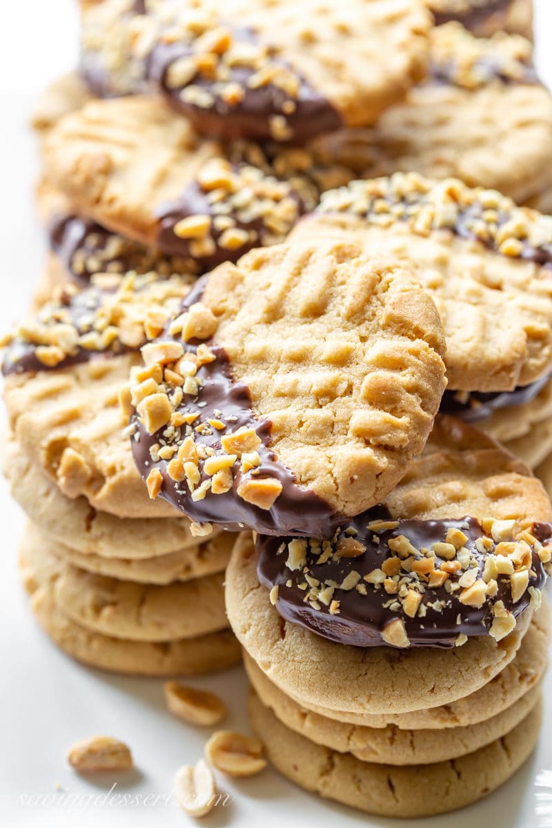 A tray of stacked peanut butter cookies, and a few cookies dipped in chocolate with chopped peanuts