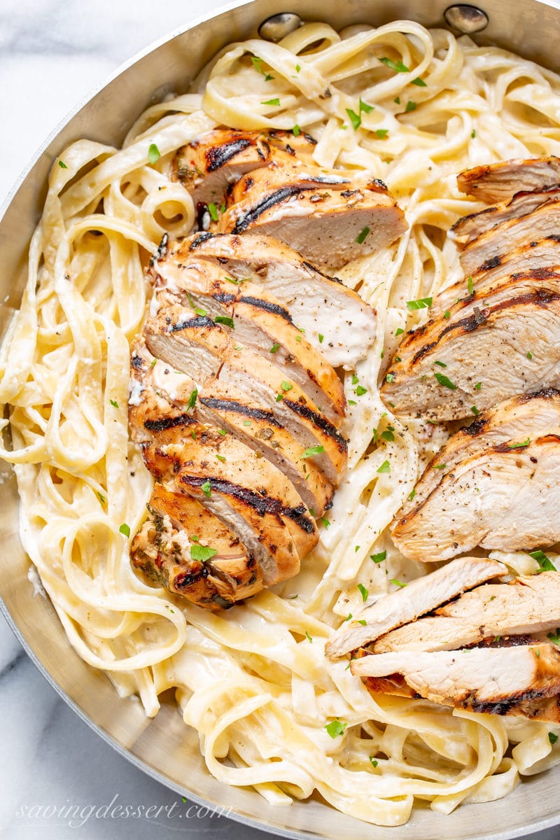 Sliced grilled chicken breasts on a skillet of creamy fettuccine Alfredo with parsley