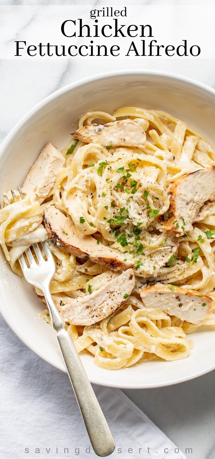 A bowl of grilled chicken fettuccine Alfredo with parsley and grated Parmesan cheese