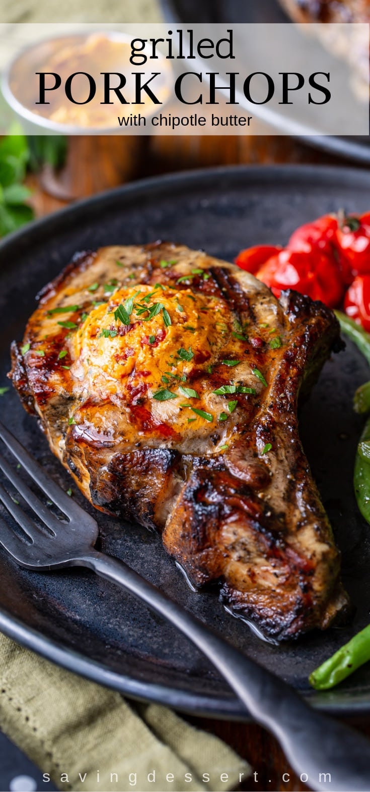 A grilled pork chop on a plate with green beans and roasted tomatoes