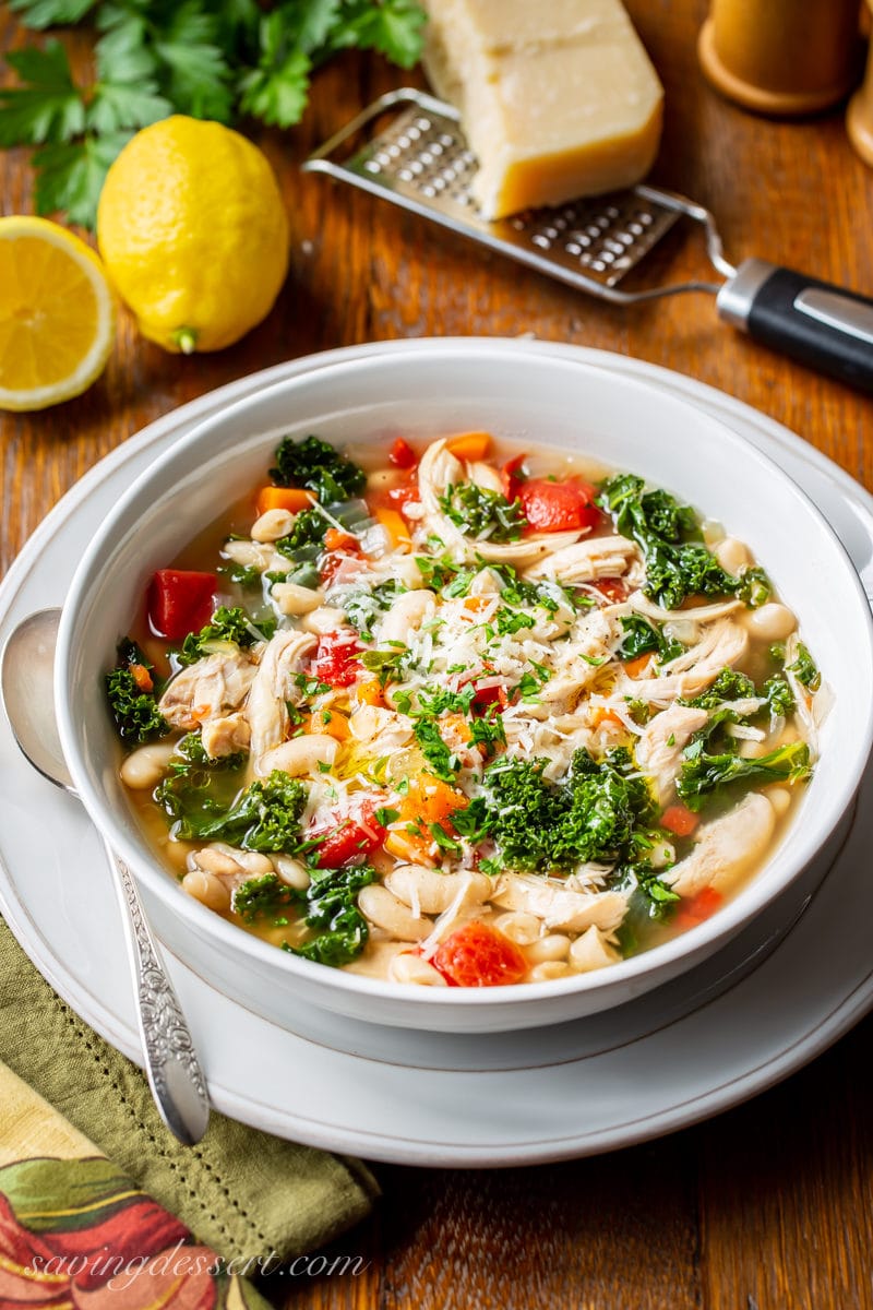 A bowl of Chicken & White Bean Soup with kale topped with fresh grated Parmesan and parsley