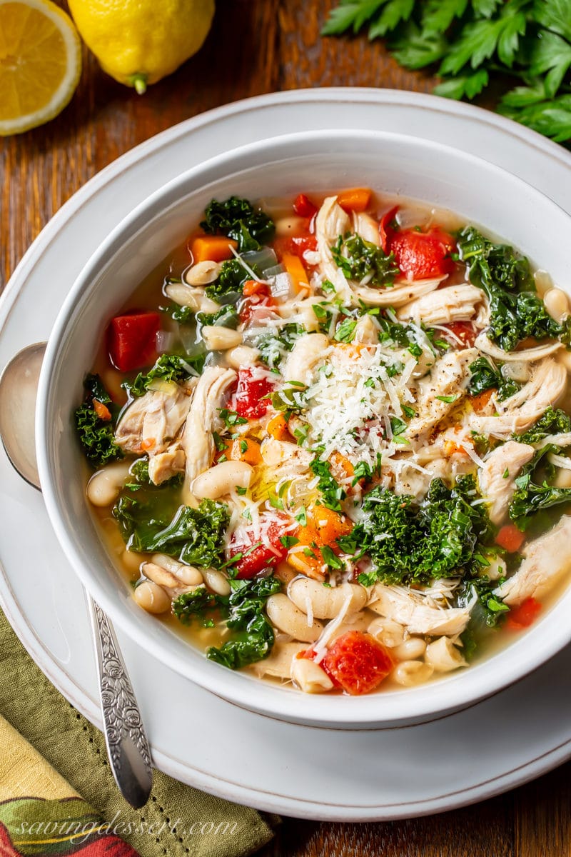 A bowl of Chicken & White Bean Soup with kale, carrots and onions topped with Parmesan