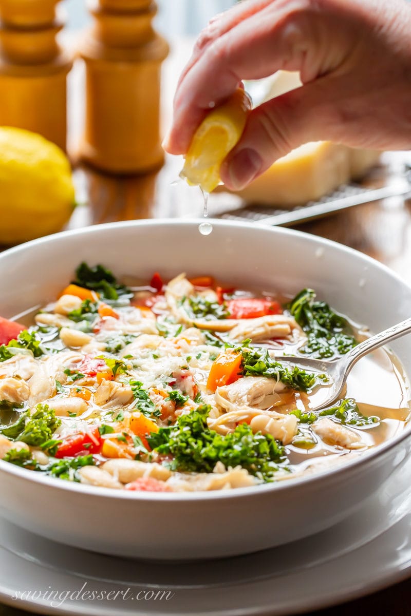A bowl of chicken & White Bean Soup with kale and tomatoes topped with Parmesan and a squeeze of lemon juice