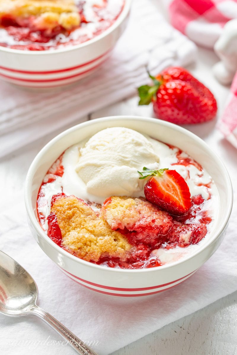 A bowl of strawberry cobbler topped with ice cream and a fresh sliced berry
