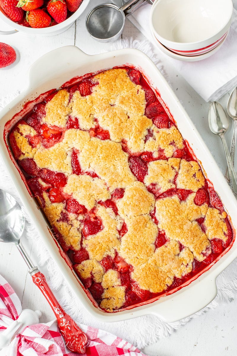 A casserole dish filled with a juicy strawberry cobbler with a crumbled biscuit topping