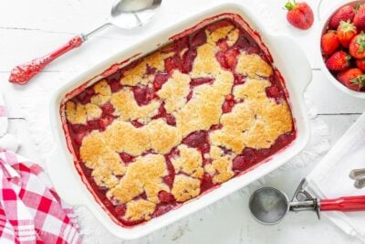 A casserole dish filled alongside a juicy strawberry cobbler alongside a crumbled biscuit topping Easy Strawberry Cobbler