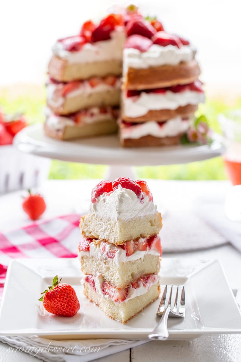 A three layer strawberry shortcake cake sliced into a towering wedge with fresh red ripe strawberries and layers of whipped cream