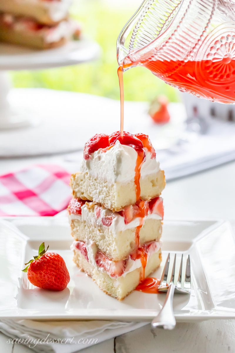 A slice of three layer strawberry shortcake cake drizzled with strawberry syrup