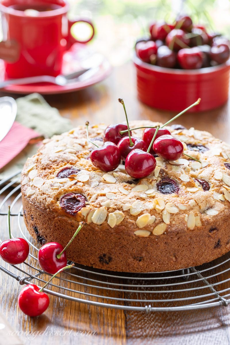 A single layer cherry breakfast cake on a rack with fresh cherries on top