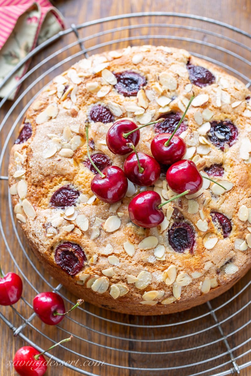An overhead view of a cherry breakfast cake topped with sliced almonds and fresh cherries