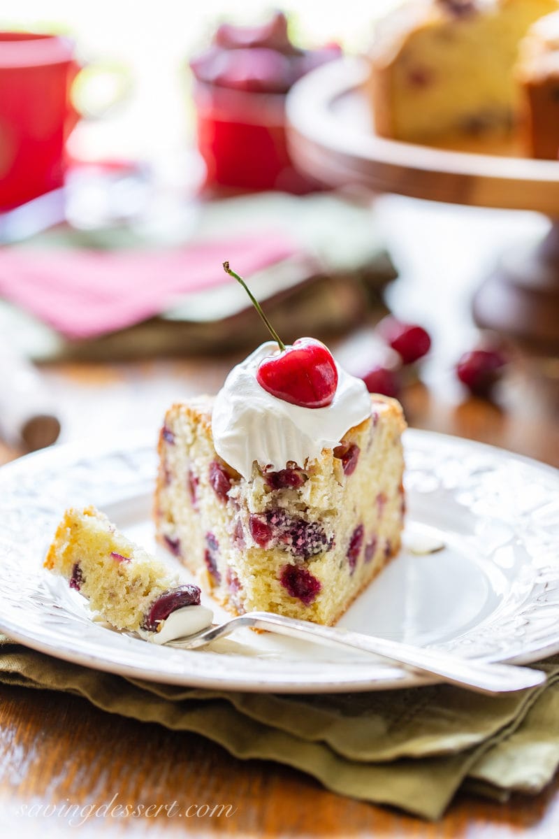 A slice of cherry almond breakfast cake with a dollop of whipped cream and a fresh cherry garnish