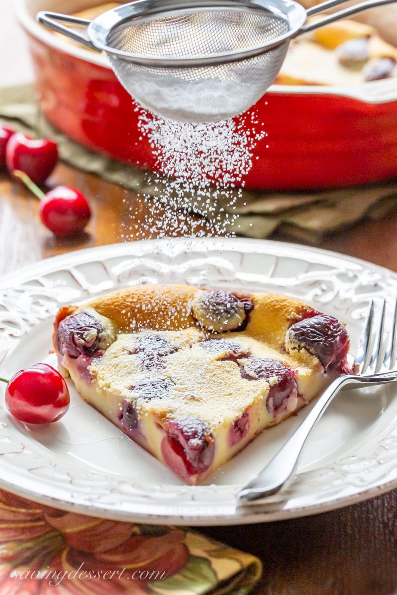 A slice of Cherry Clafoutis being dusted with powdered sugar